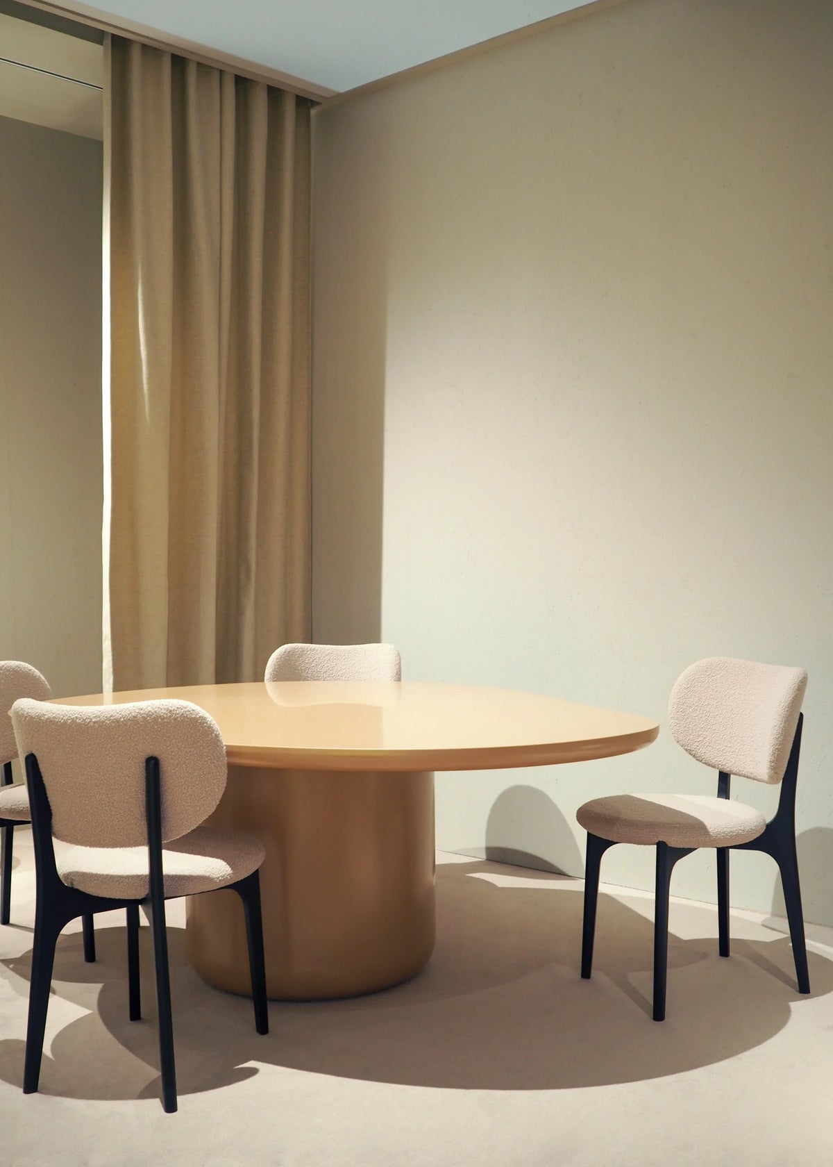 Round wood dining table with upholstered dining chairs in a neutral room with beige curtains