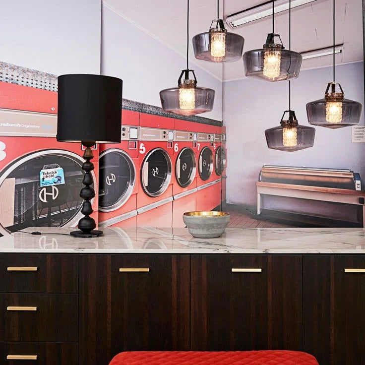 Smoked glass pendant lights hung in clusters over a marble counter in a retro laundromat-style interior
