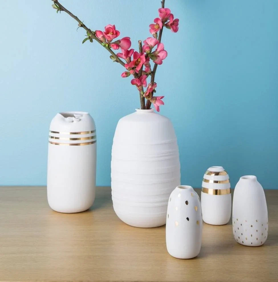 White ceramic vases with gold stripes and blossom branches on a wooden shelf