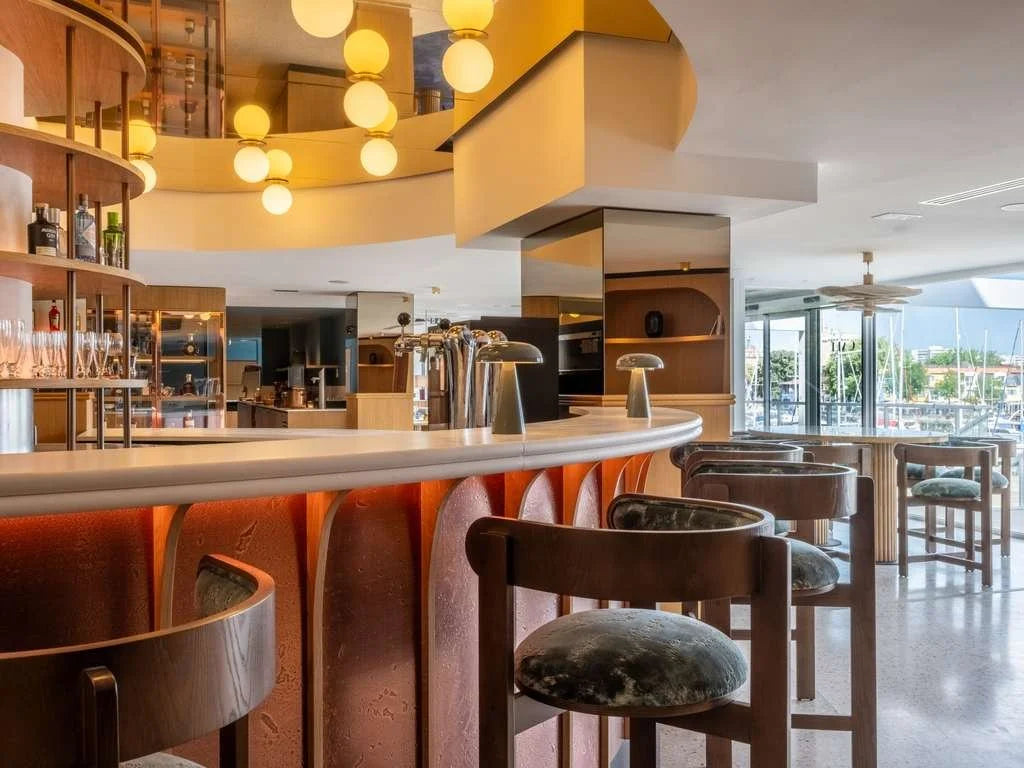 Moulin Counter Stool with patterned seats at a curved bar under globe lights