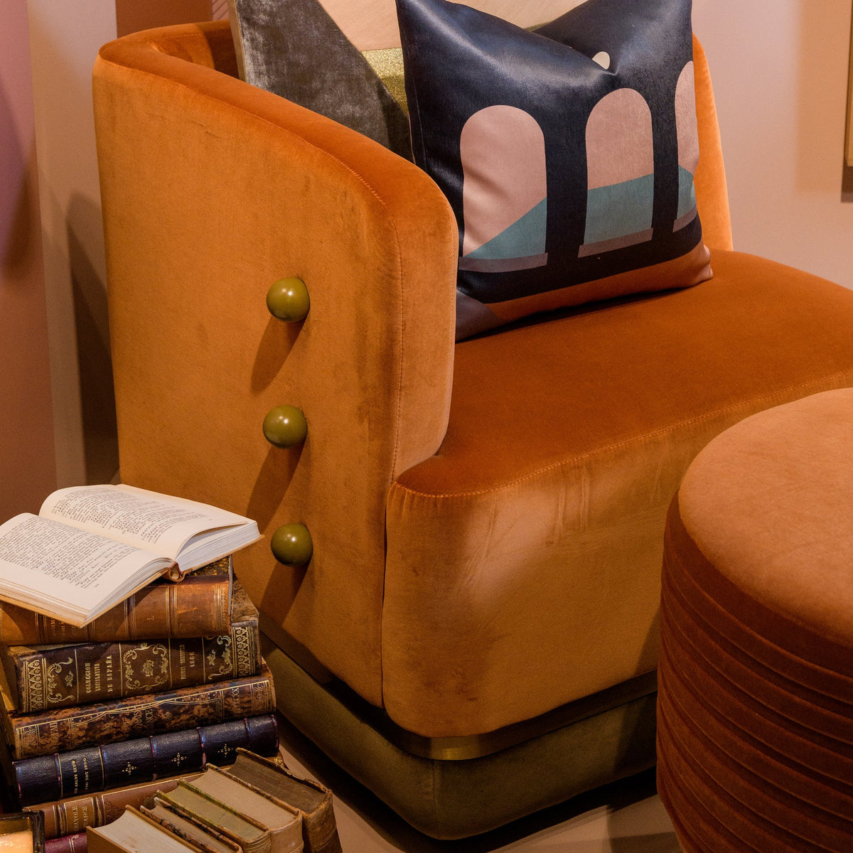 Panorama Armchair in orange velvet with patterned cushion and stacked books, close-up