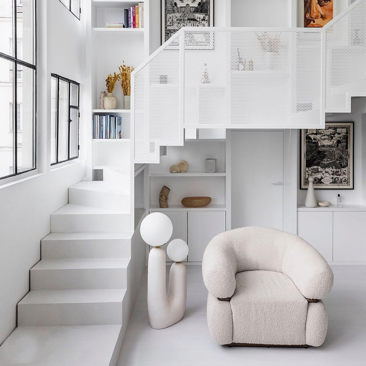 Malibu Armchair in ivory Bouclé beside a white staircase and sculptural lamp