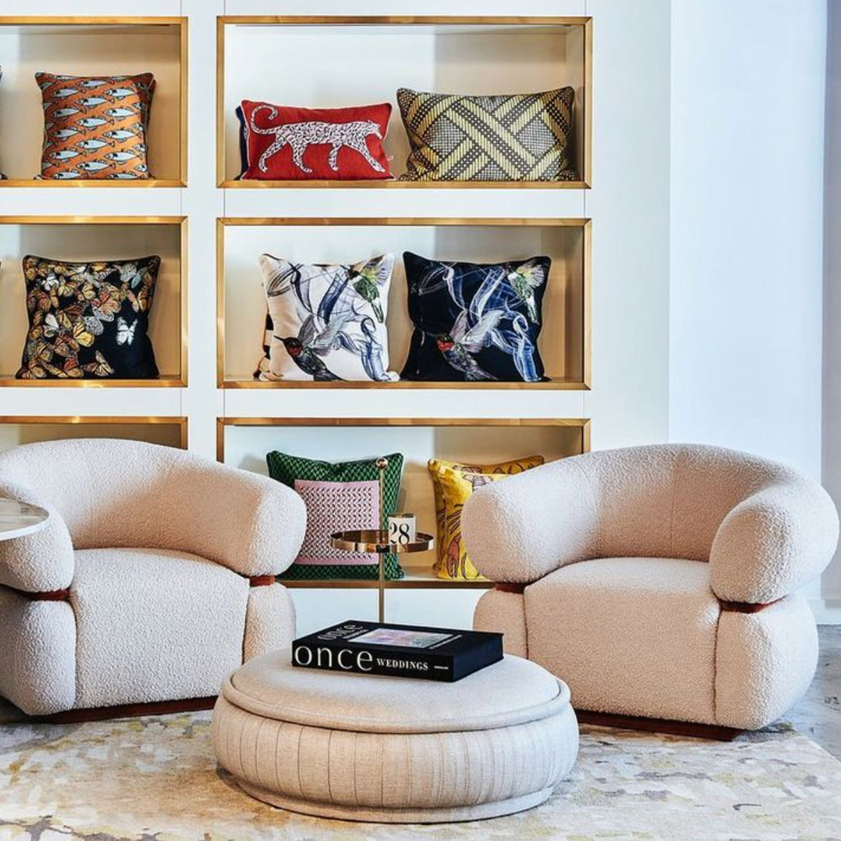 Malibu Armchair pair in ivory Bouclé before shelves of patterned cushions