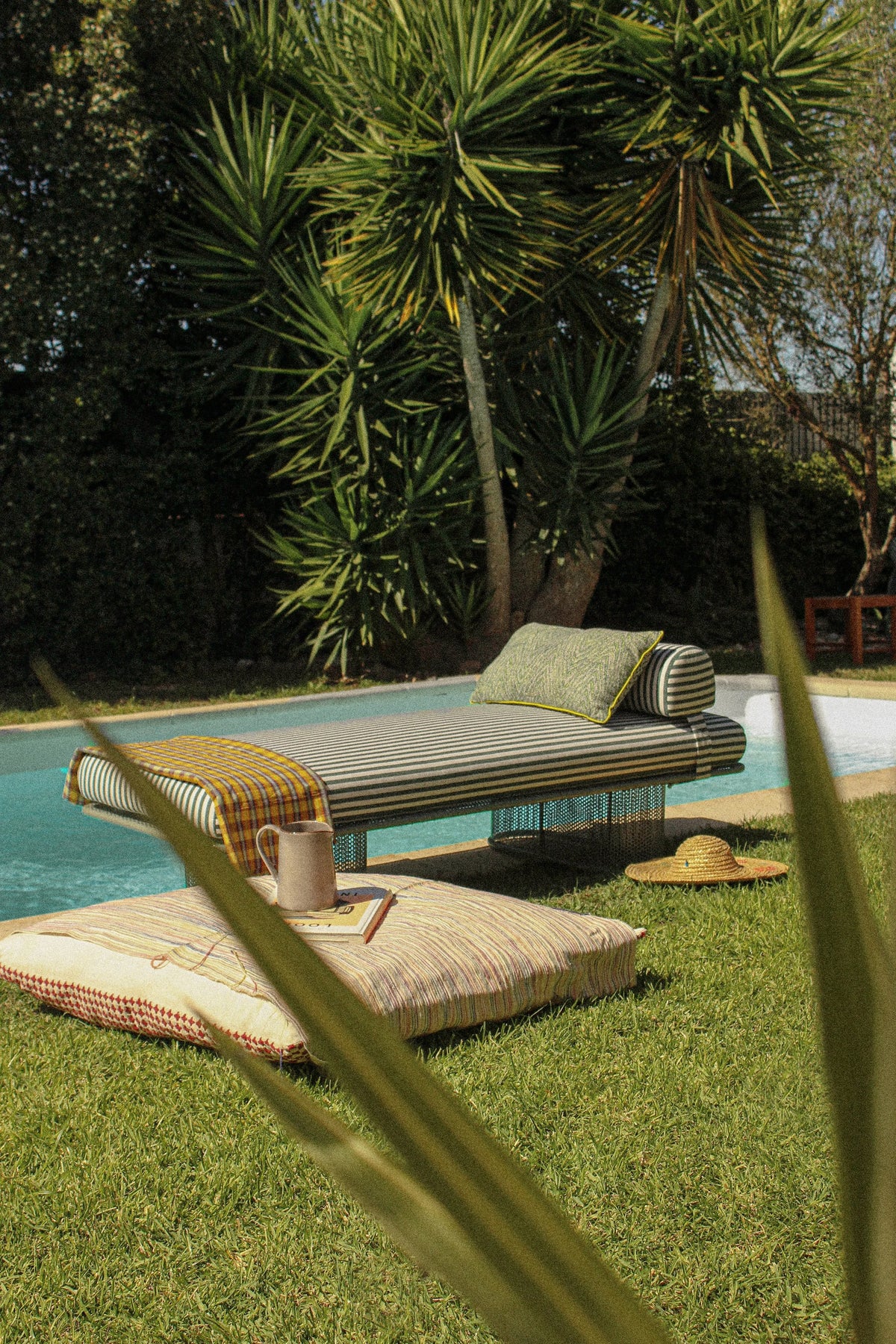 Riviera Bench with striped cushion and bolster beside a pool