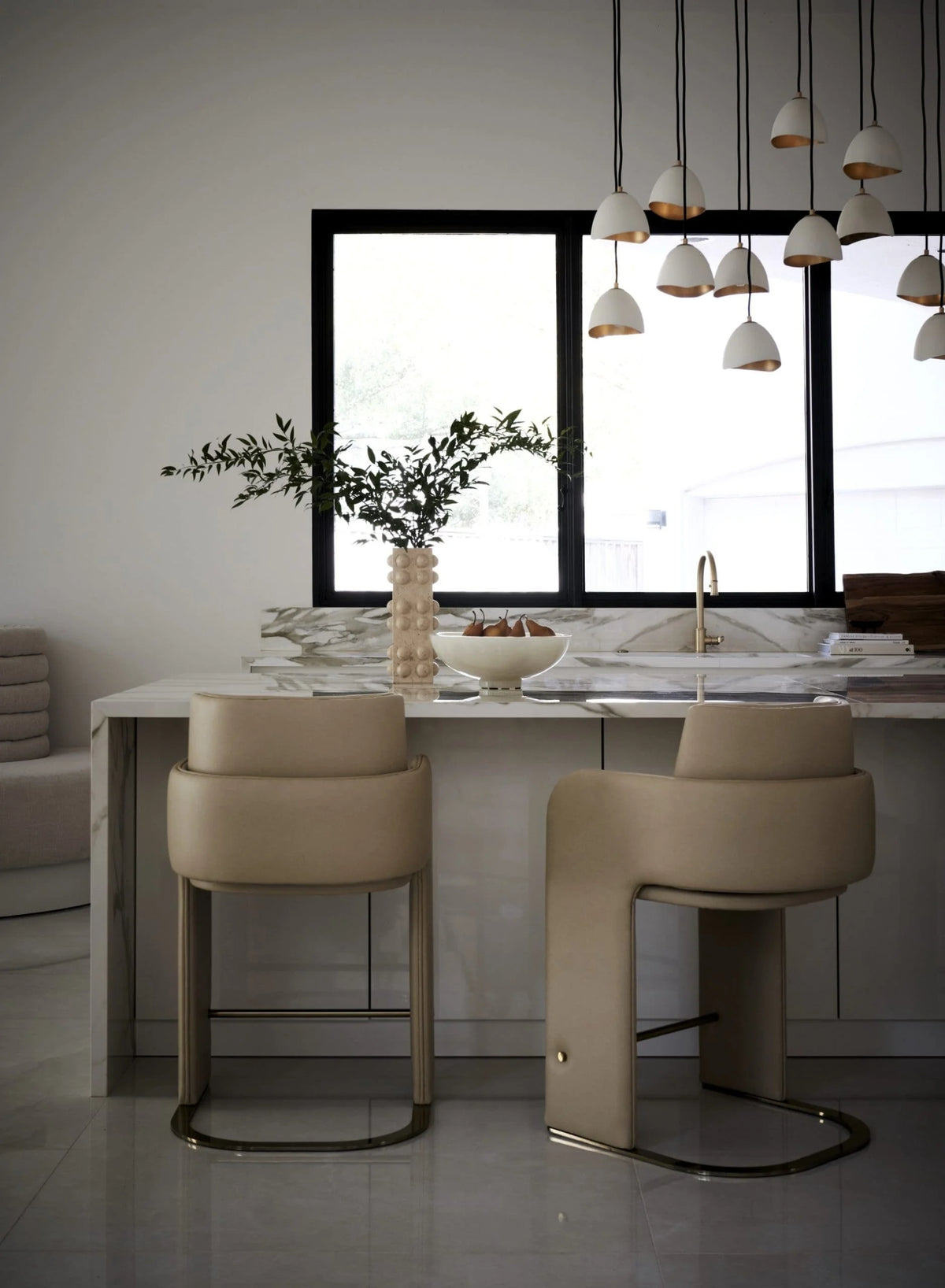 Odisseia Bar Stool pair in beige at a marble kitchen island under pendant lights