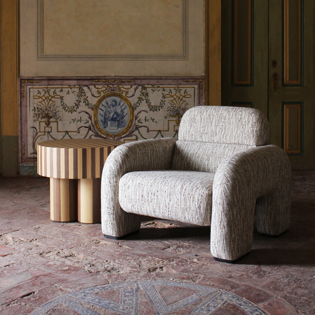 Vertigo Armchair in light grey bouclé in a frescoed room with a fluted side table