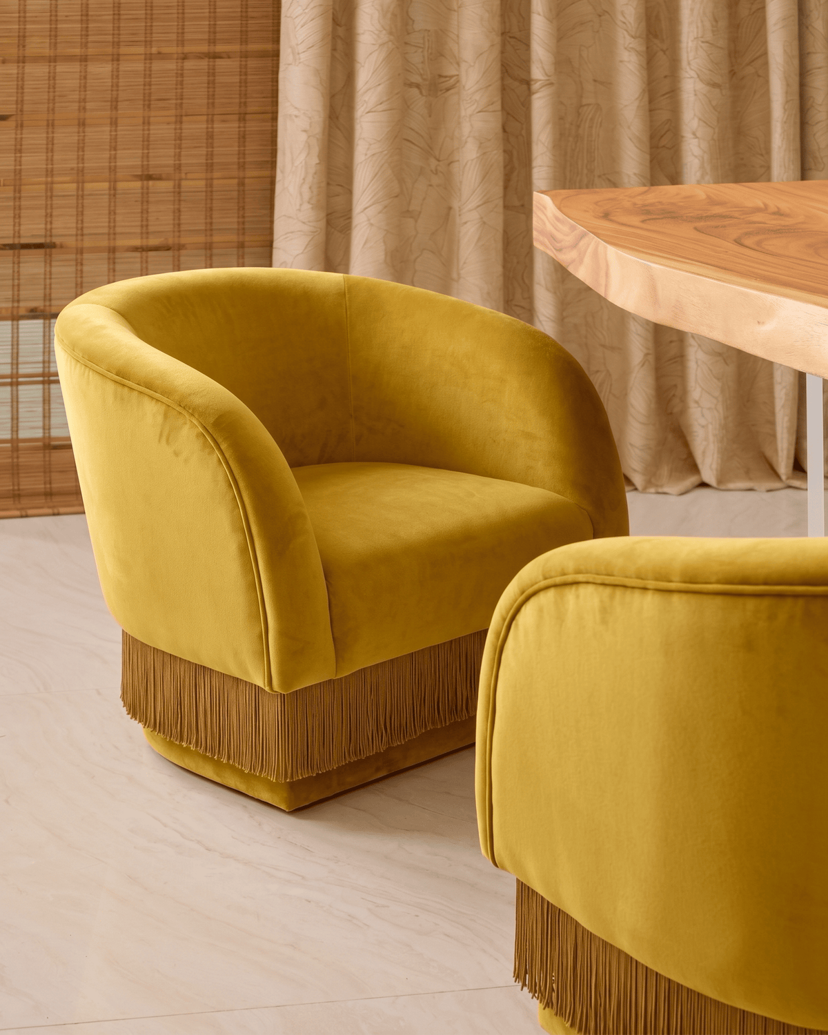 La Folie Armchair pair in mustard velvet with brown fringe beside a wood table