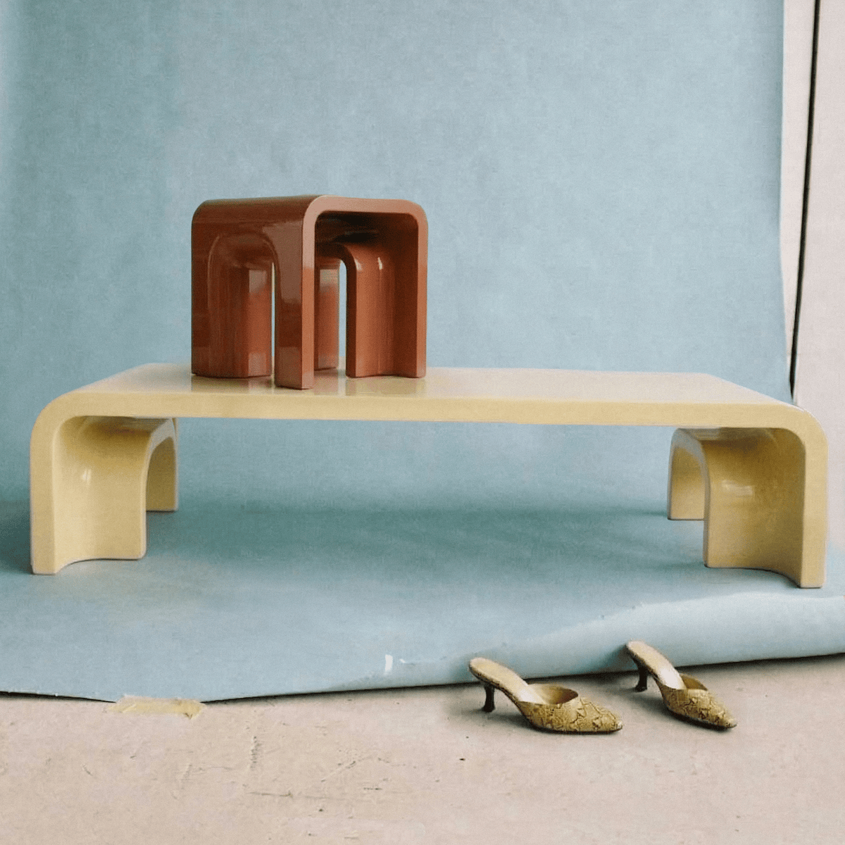 Plié Centre Table in a pale cream finish styled with a terracotta object on a blue backdrop