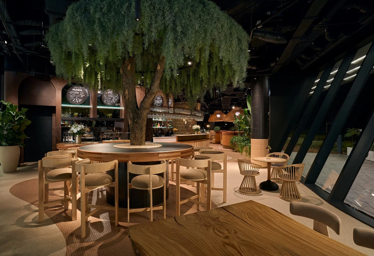 Moulin Bar Stool set around a tall table under an indoor tree in a restaurant