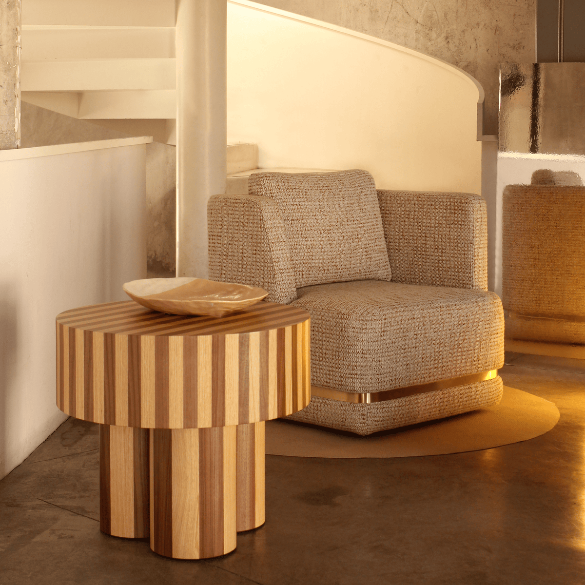 Nusa Side Table holding a bowl beside a grey upholstered armchair by a spiral stair