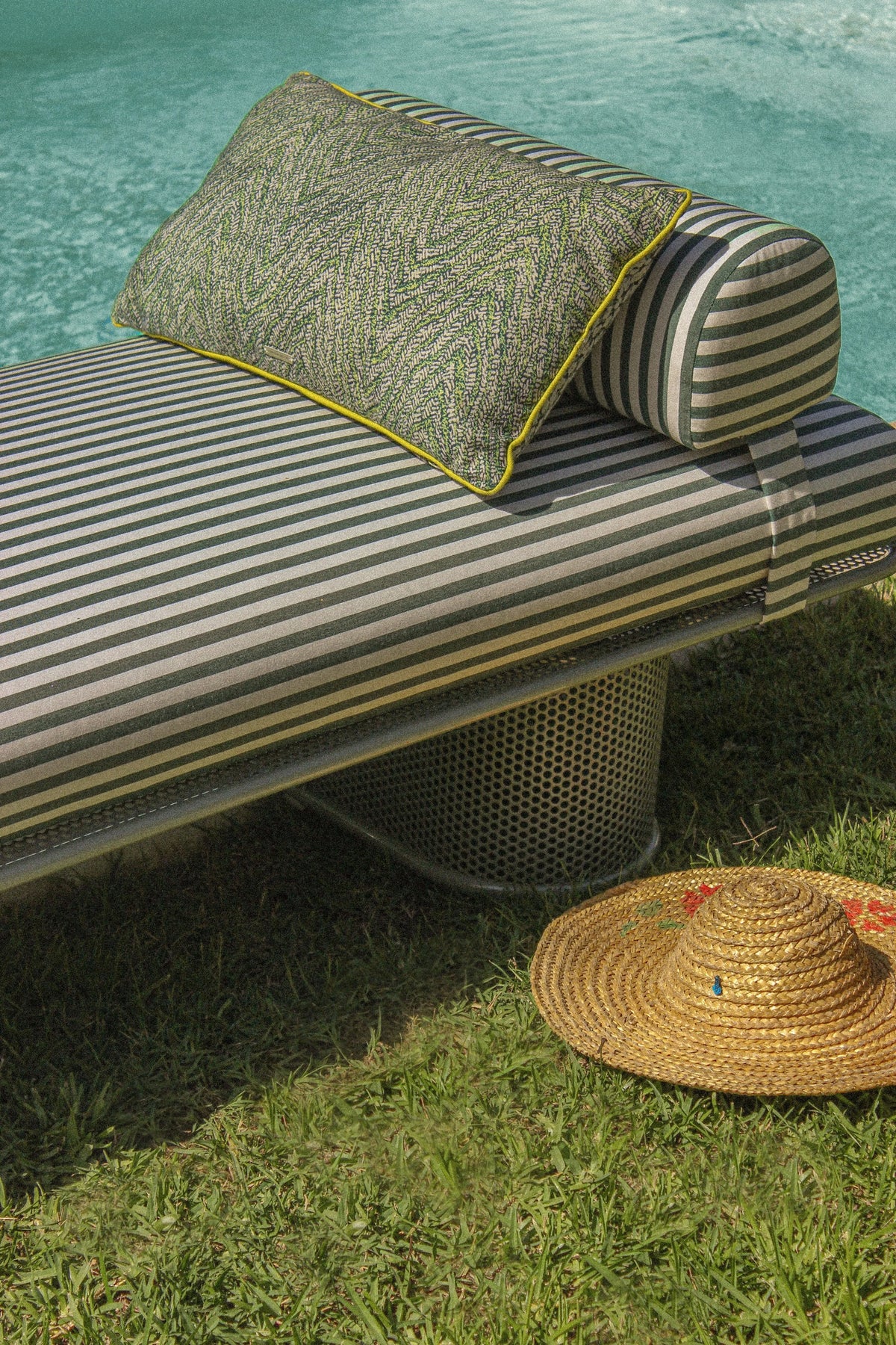 Riviera Bench in green stripes with a patterned pillow and straw hat
