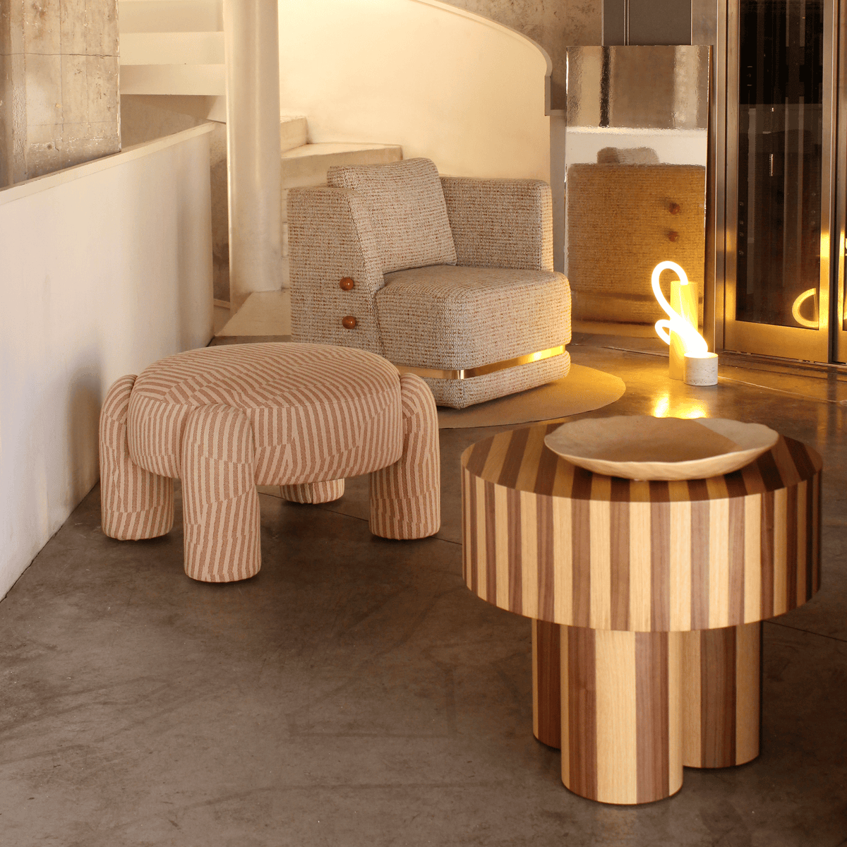 Nusa Side Table with a glowing sculpture beside a striped pouf and armchair