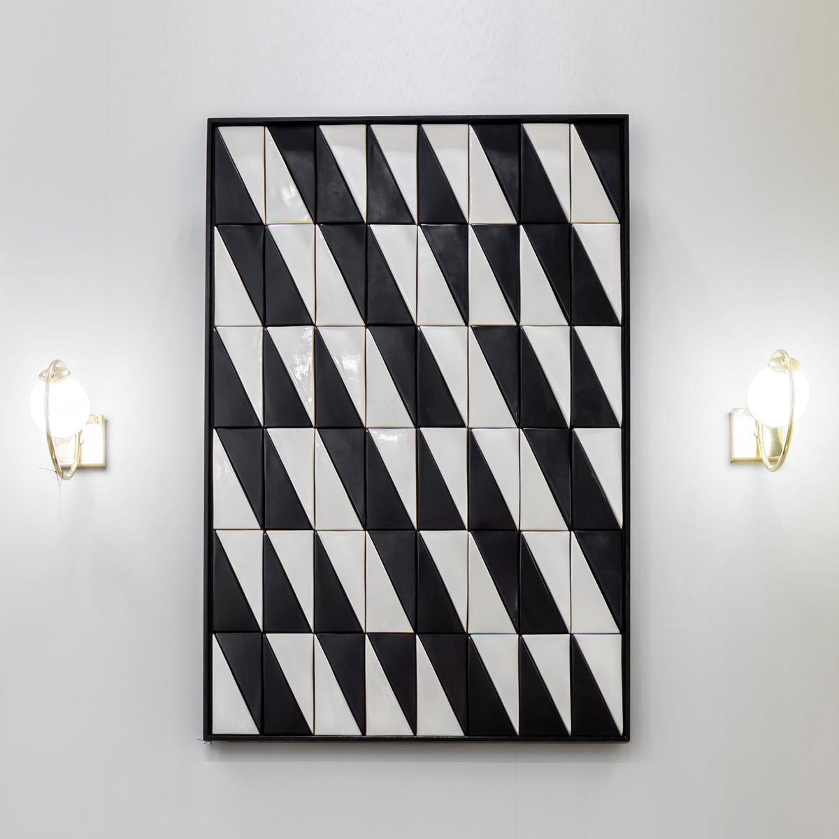 Tejo Black & White Panel hung vertically between two brass wall sconces