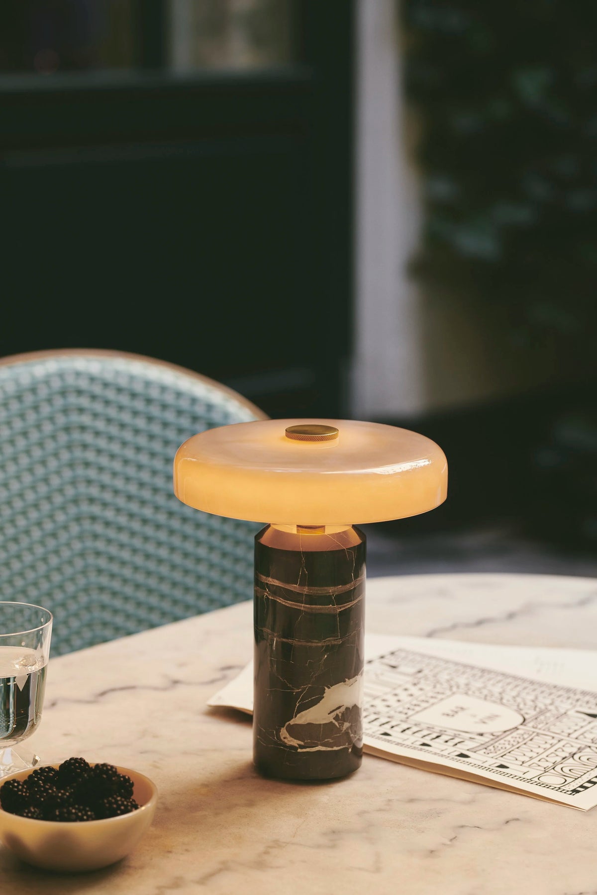 Trip Table Lamp with dark marble base lit on a café table, close-up