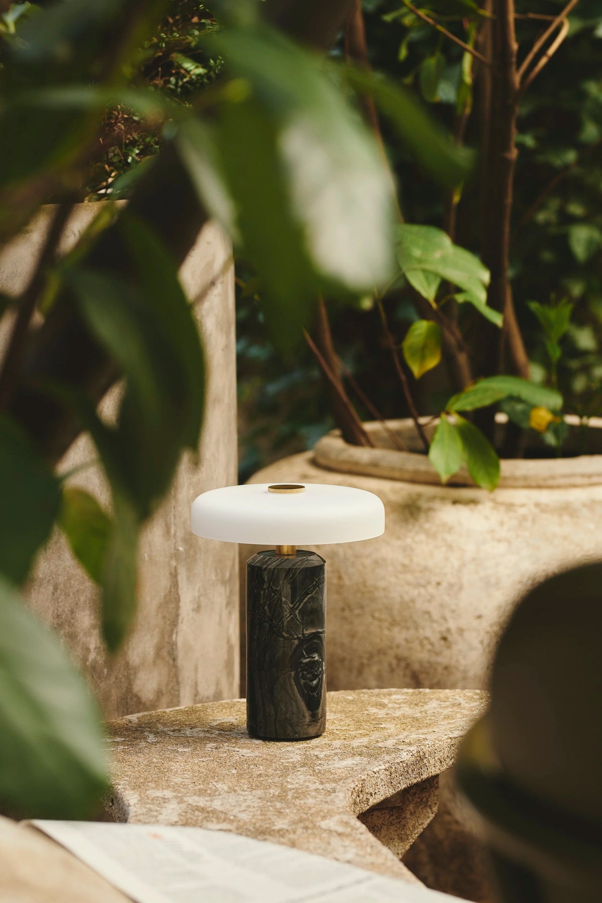 Trip Table Lamp in Charcoal and Opal on a stone ledge among garden plants