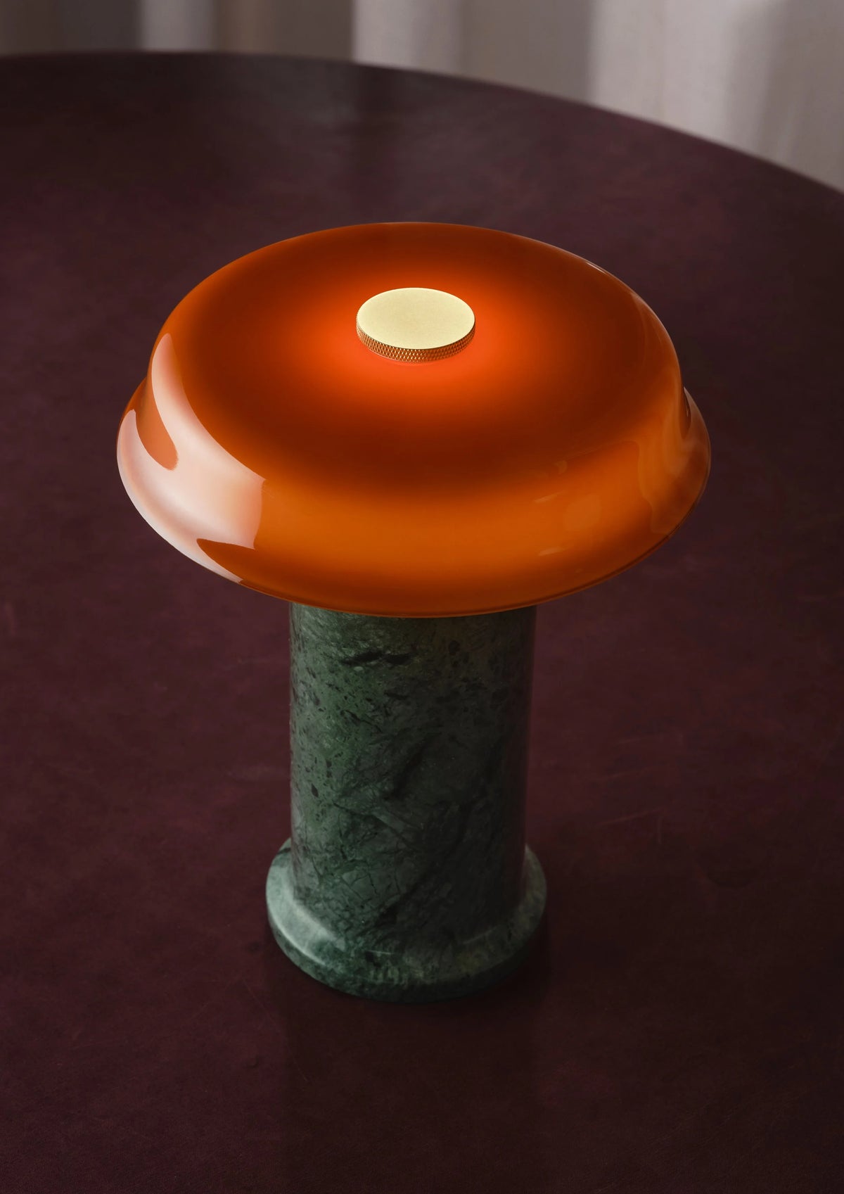 Trip 2 Table Lamp in Moss and Amber, lit, on a burgundy tabletop