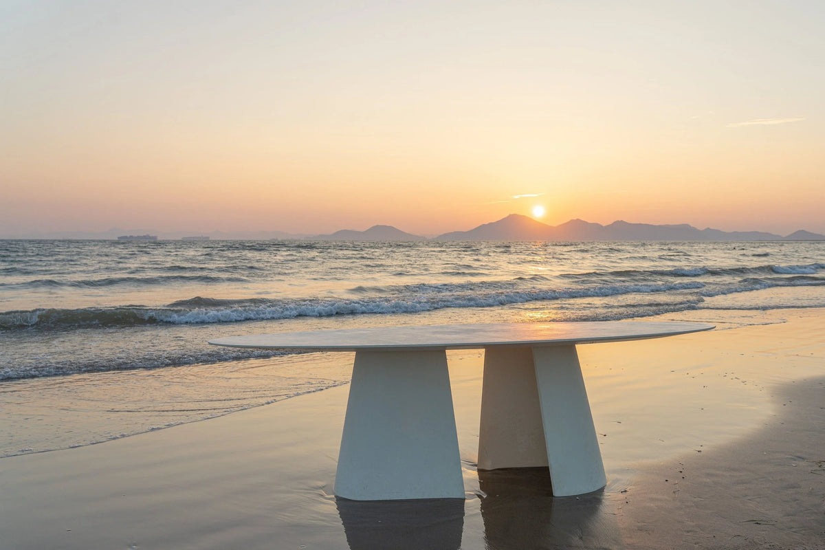 Tumuli Oval Dining Table in white on a beach at sunset