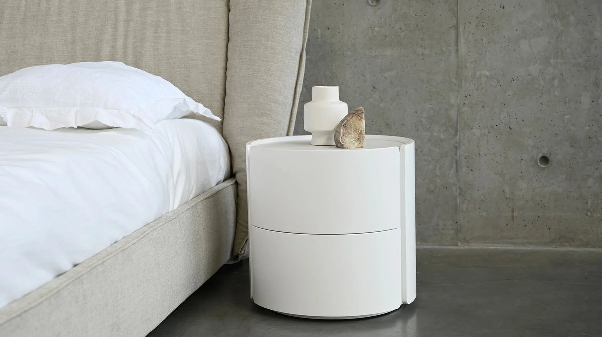 Burrow white round night table beside an upholstered bed against a concrete wall