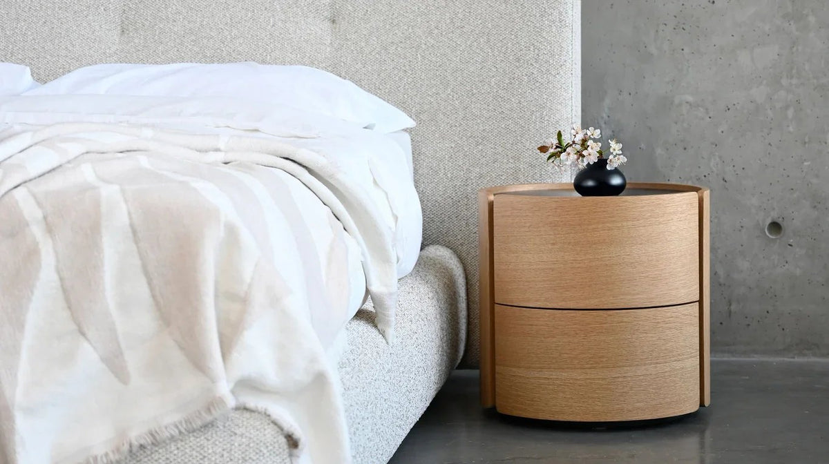 Burrow Night Table in Oak & Black Stone Top beside a bed on a concrete floor