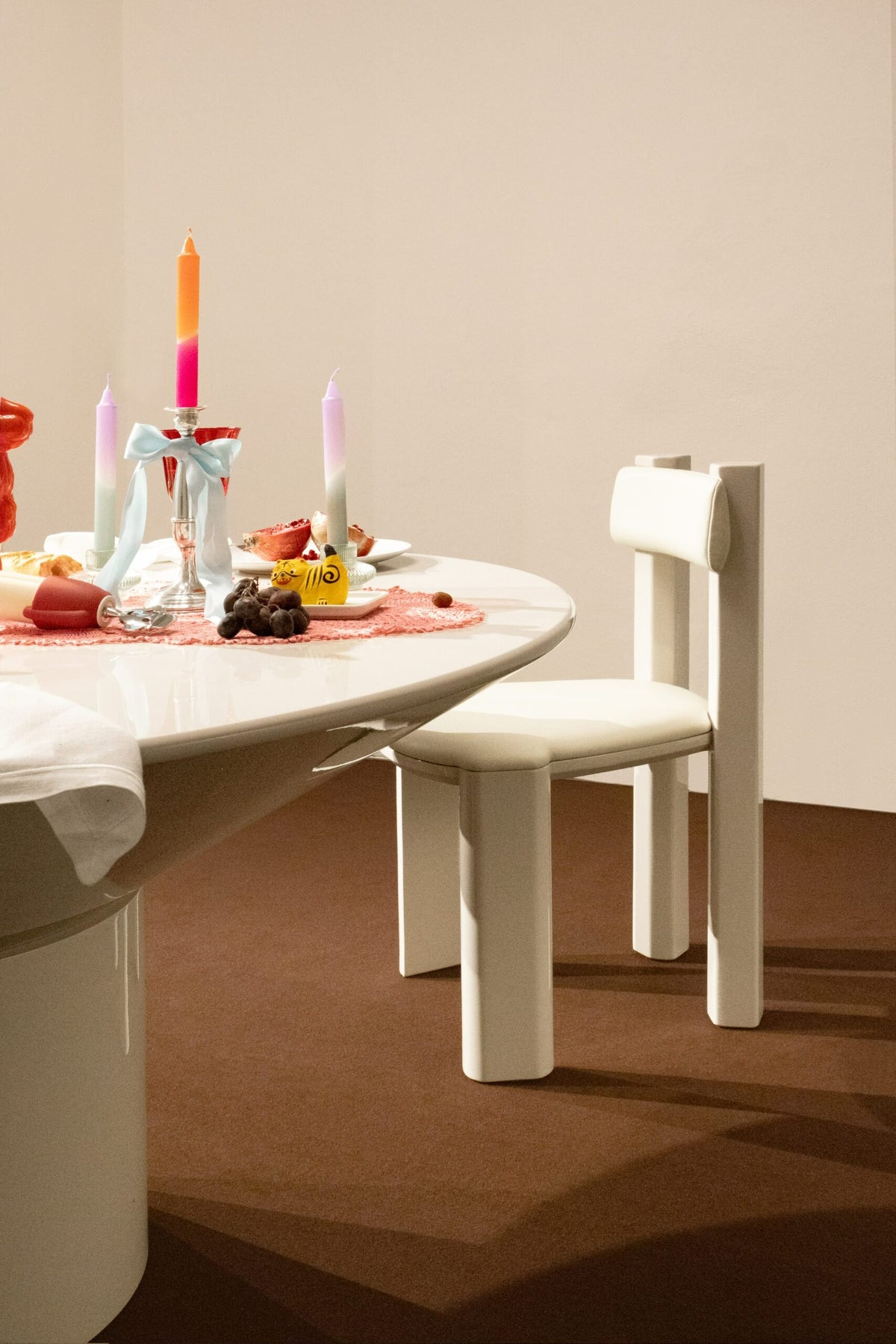 Silo Dining Table in off-white lacquer set with candles beside a cream wood chair