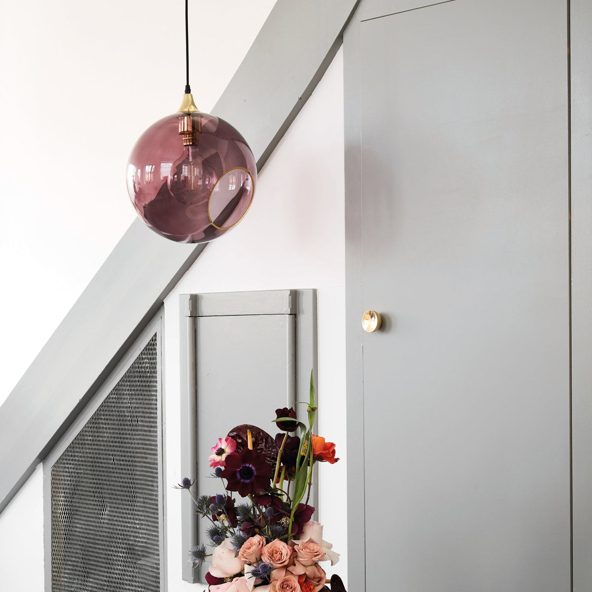 Ballroom XL Purple Rain Pendant Light hanging beside a grey staircase above a flower arrangement