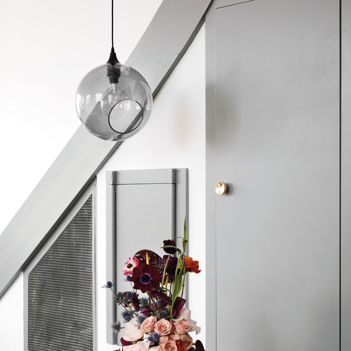 Ballroom XL Smoke Pendant Light hanging in a grey stairwell above flowers