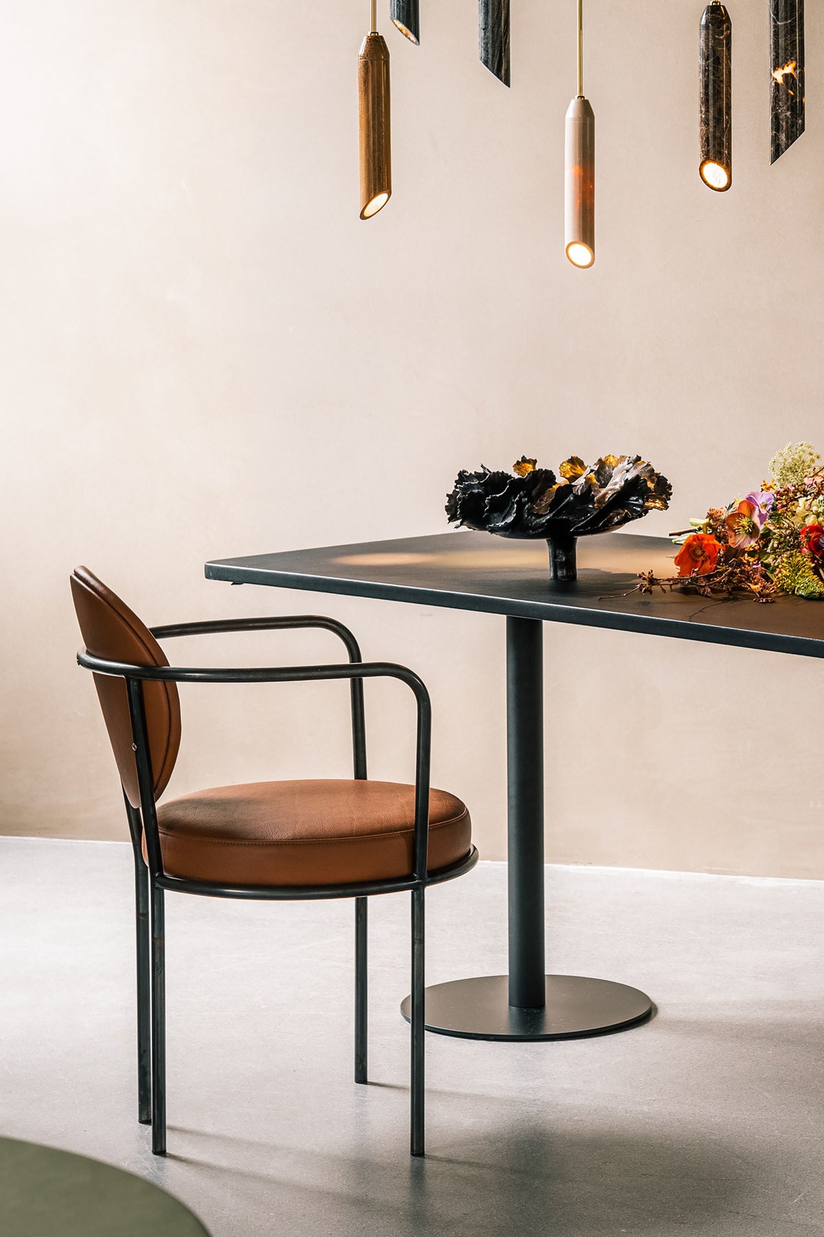 Casablanca Chair in Cognac Leather at a black pedestal table with brass pendants and flowers