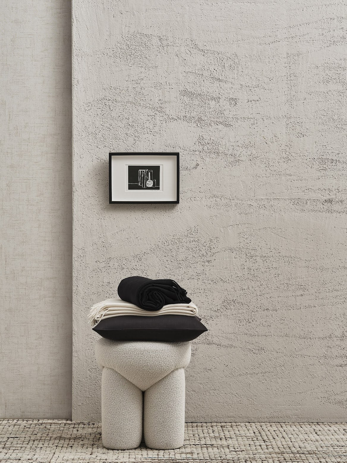 Douglas Ottoman in cream bouclé topped with folded black throws