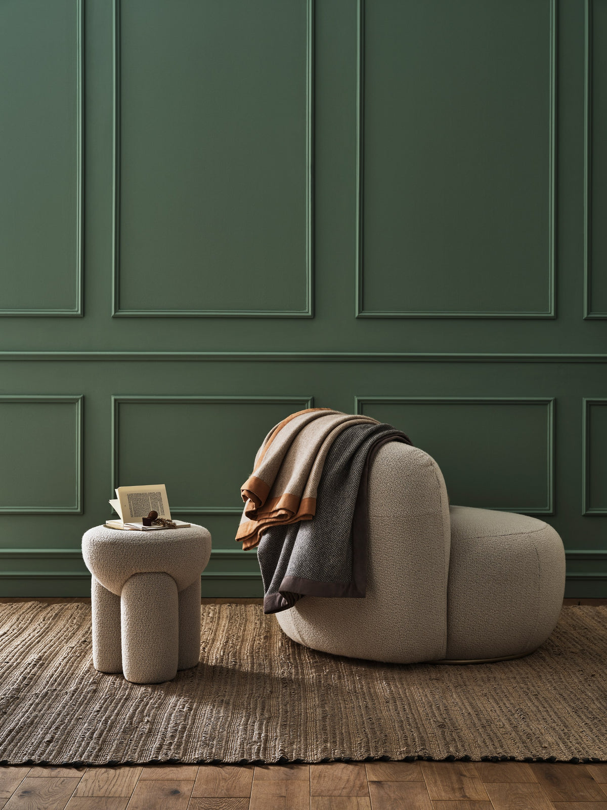 Douglas Ottoman in cream beside a lounge chair against green panelling