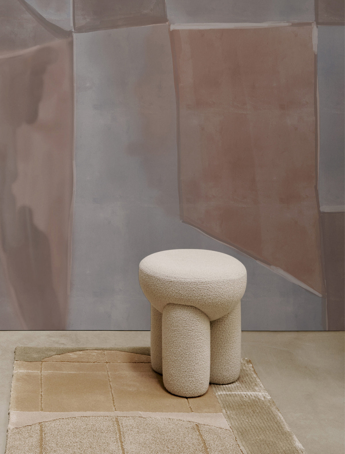 Douglas Ottoman in cream bouclé on a rug before a painted wall