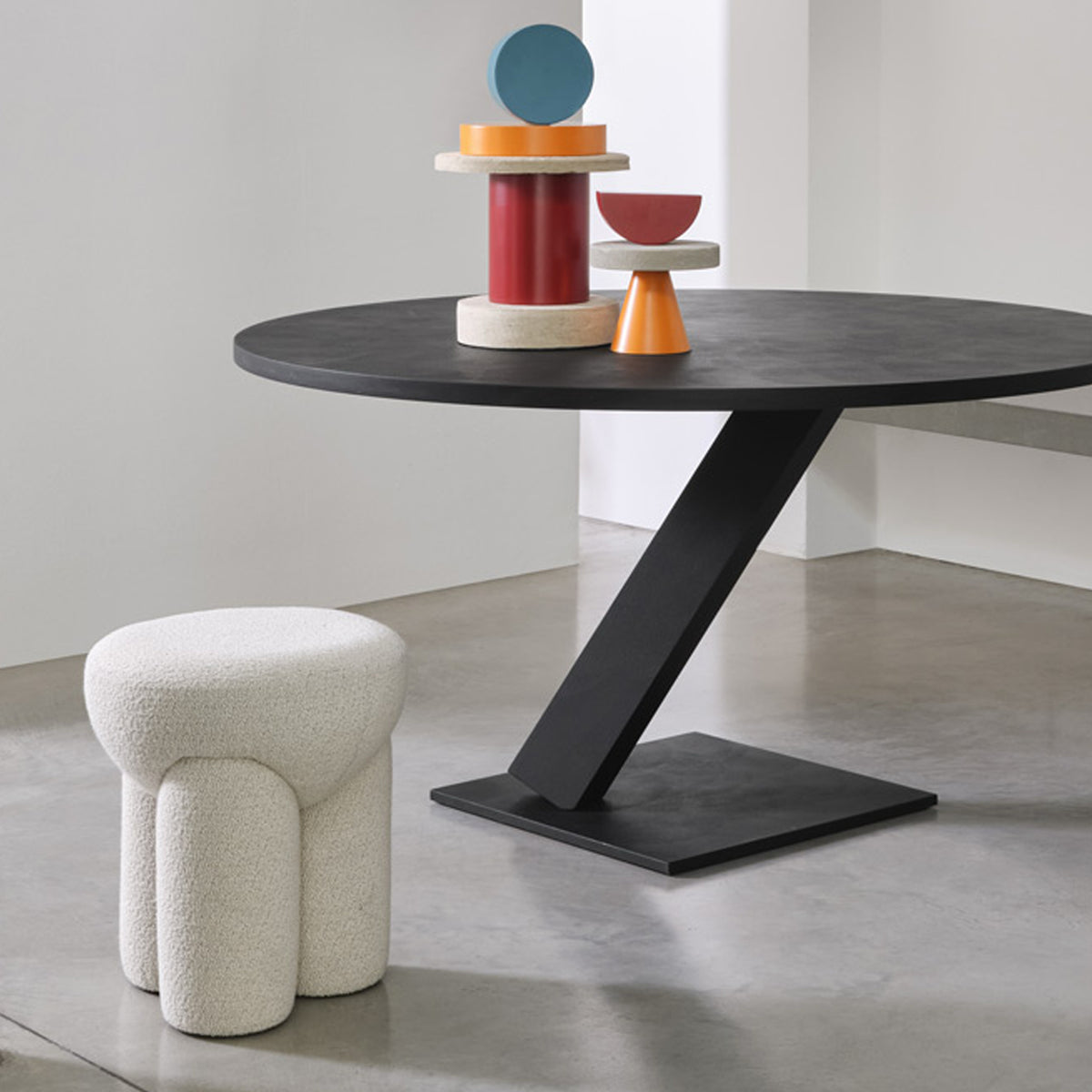 Douglas Ottoman in cream bouclé beside a black table with sculptures