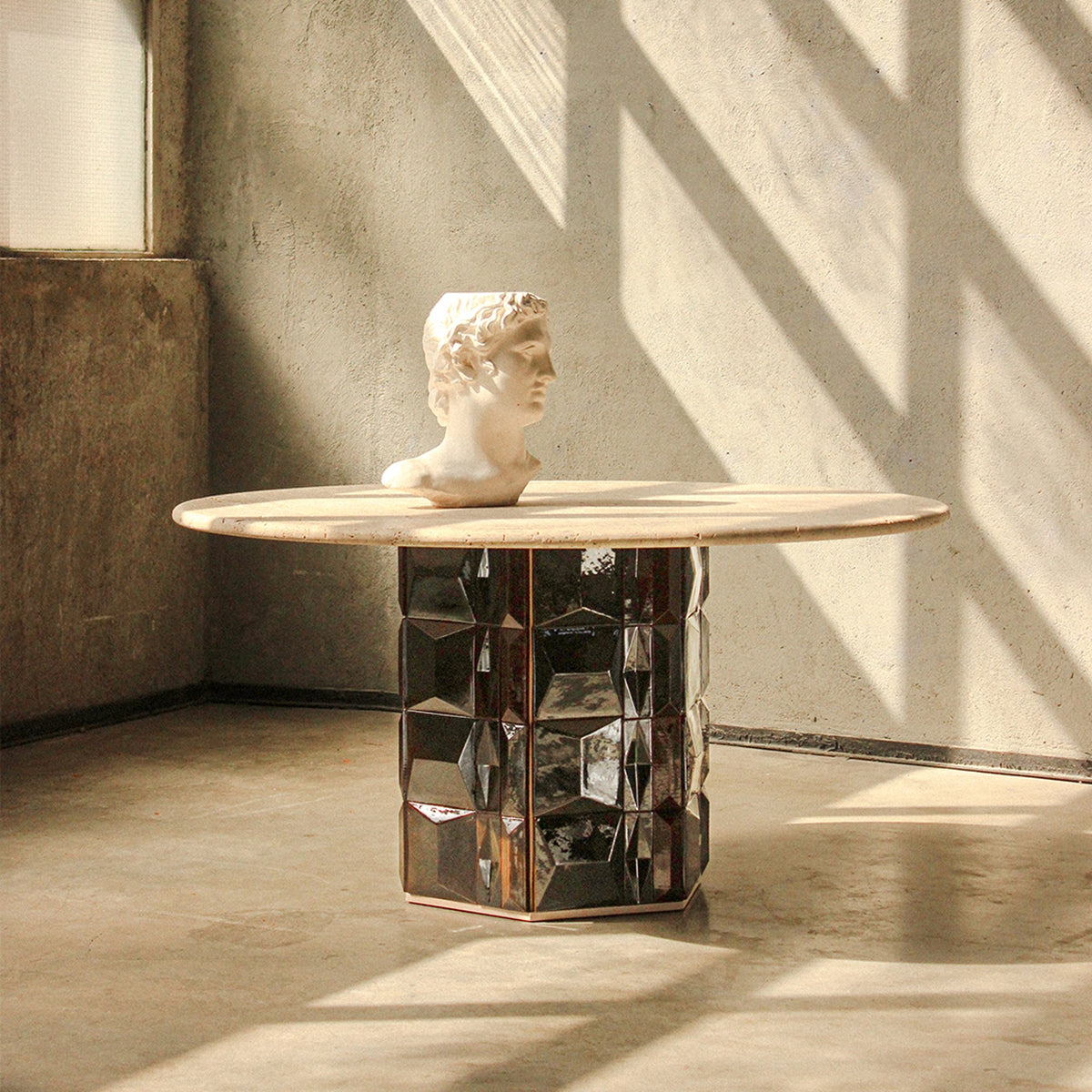 Milano Dining Table with a classical bust in a sunlit concrete room