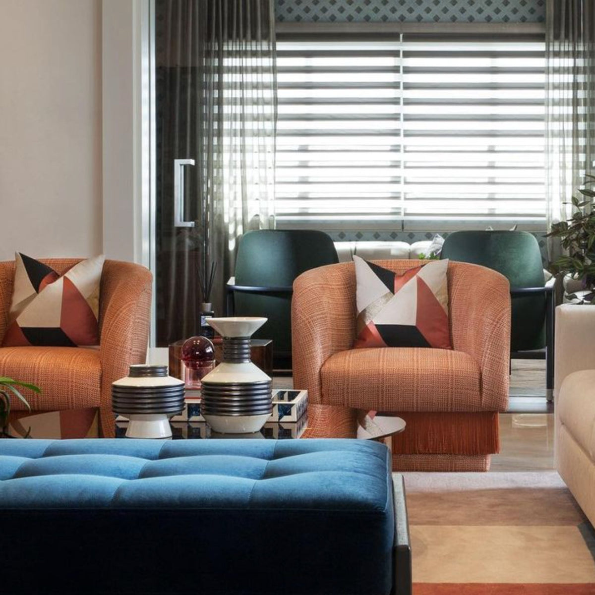 La Folie Armchairs in coral with geometric pillows around a blue tufted ottoman