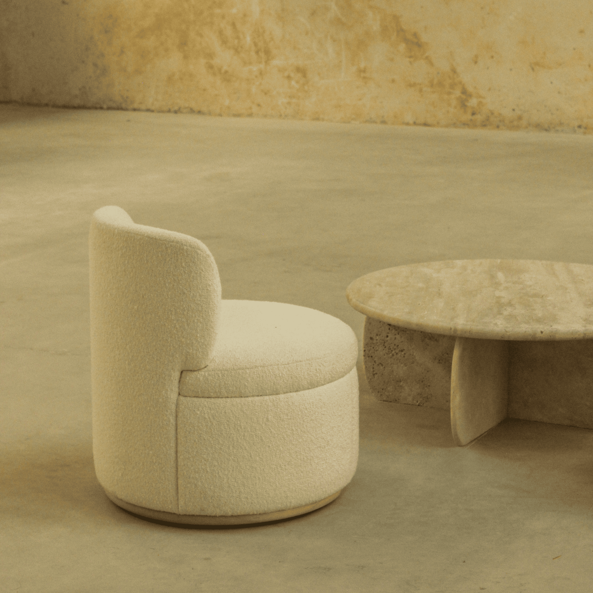 Mimi Swivel Lounge Chair in cream bouclé beside a travertine table, back three-quarter view