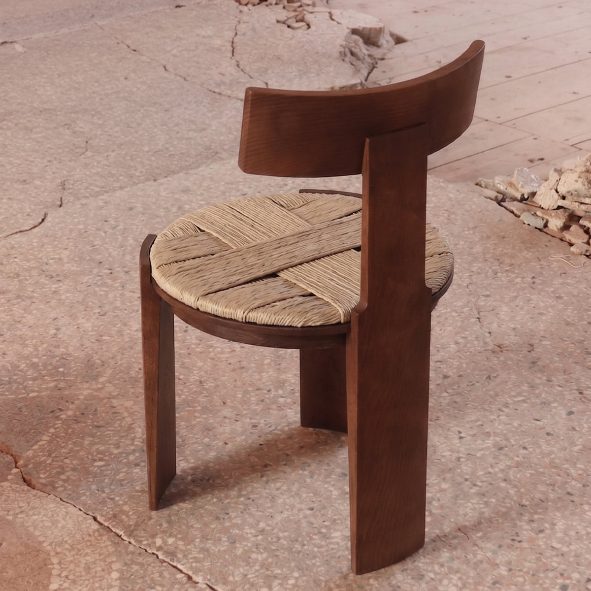 Nest Dining Chair in dark ash with woven rush seat on a cracked earth floor