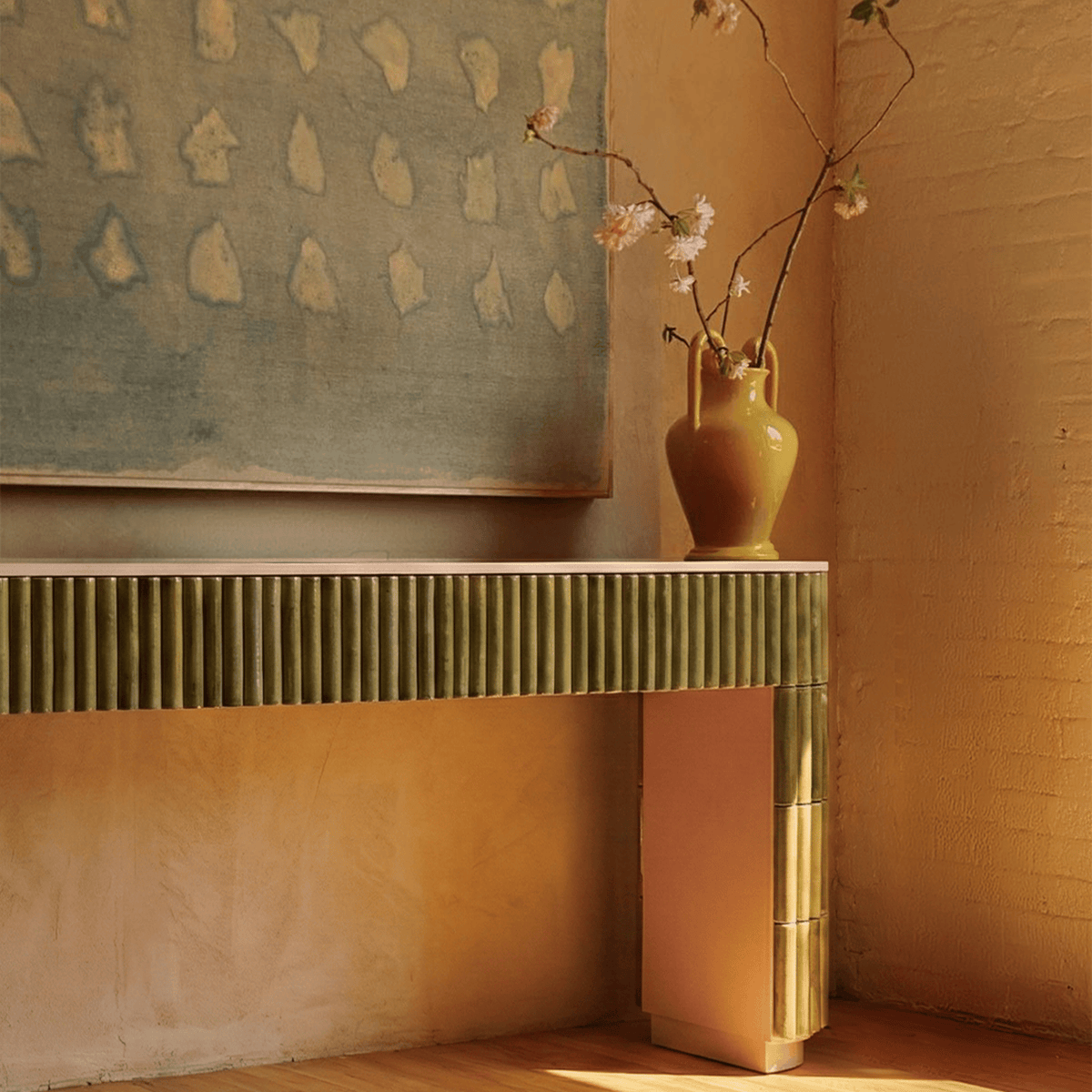Nouvelle Vague Console Table in green tiles in a terracotta room with a vase of blossoms