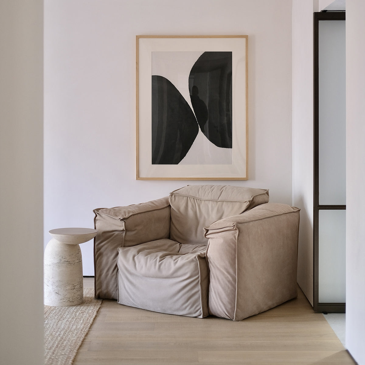Pingu X Side Table in Travertino beside a leather armchair under black and white art
