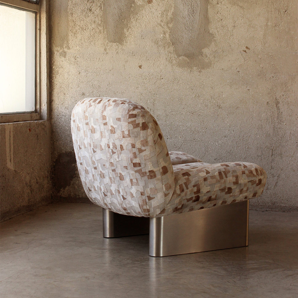Colin Armchair in geometric jacquard, rear three-quarter view in a concrete loft
