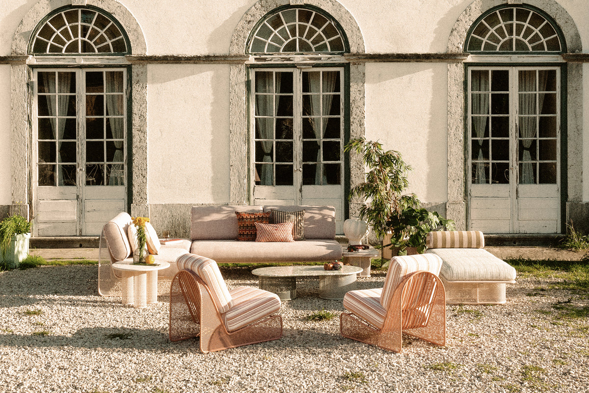 Riviera Bench in an outdoor lounge set on gravel before arched windows