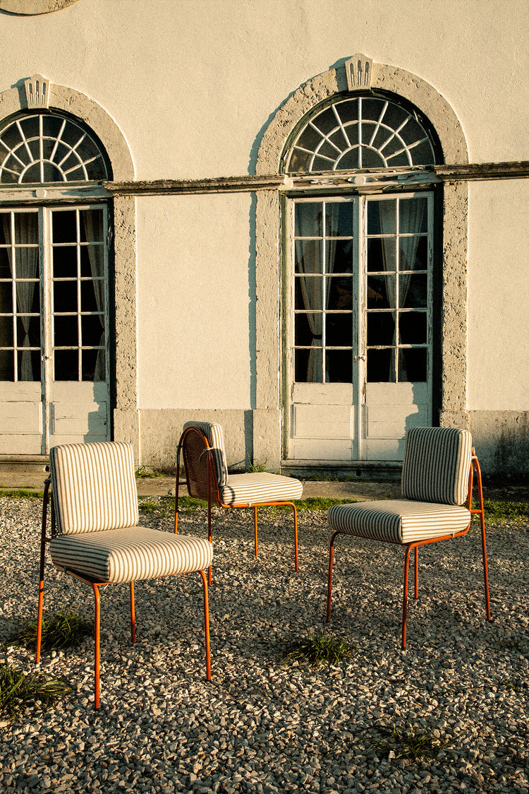 Riviera Chairs in stripe upholstery on gravel before arched windows