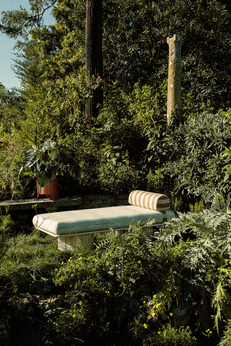 Riviera Vases in a lush garden beside a striped daybed