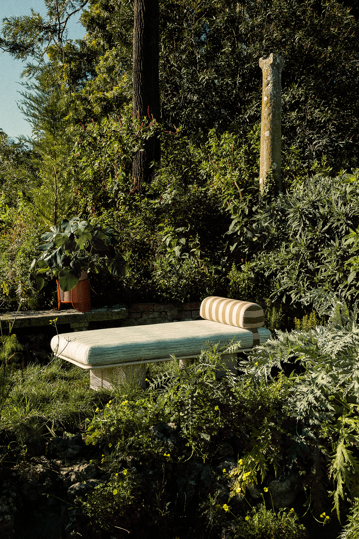 Riviera Bench with striped bolster among lush garden plants