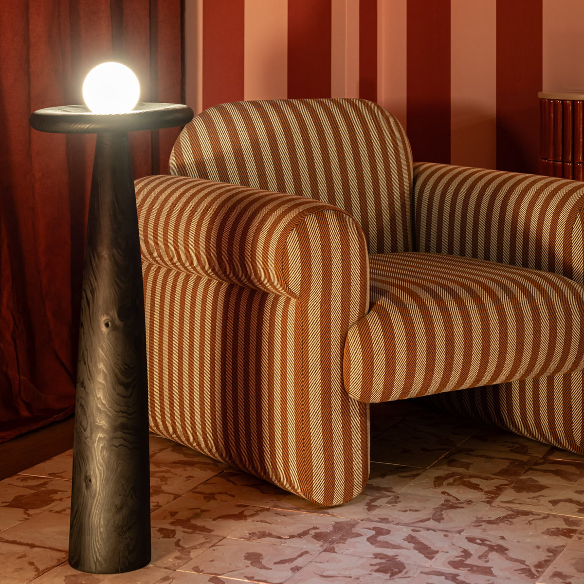 Oscar Armchair in ochre stripes beside a dark floor lamp in a red-striped room