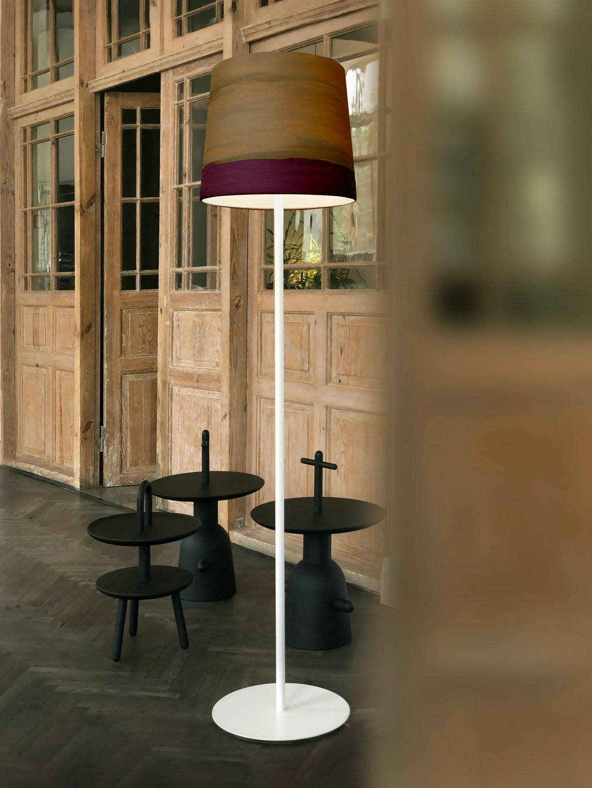 Mammalampa Sisters Floor Lamp in Twilight beside black side tables and wooden doors