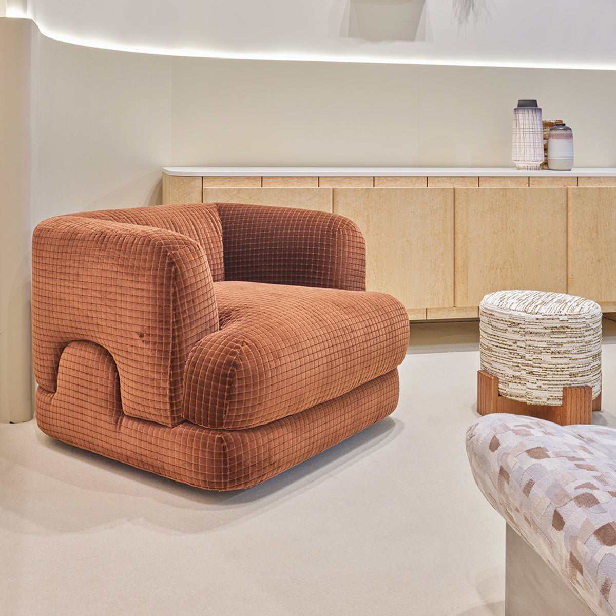 Mosaico Armchair in rust grid velvet in a showroom with a white stool