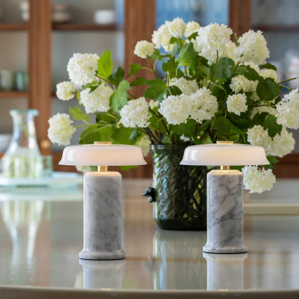Trip 2 Table Lamps in Carrara and Opal on a glass table with white hydrangeas