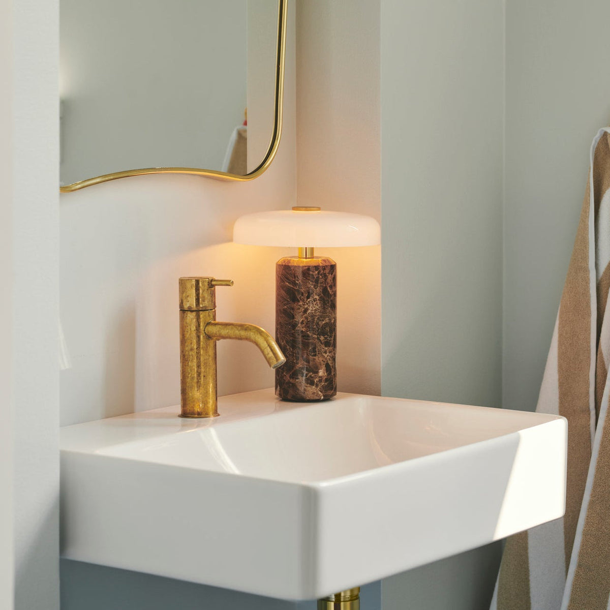Trip Table Lamp in Dark Emperador / Opal on a bathroom sink beside a brass tap