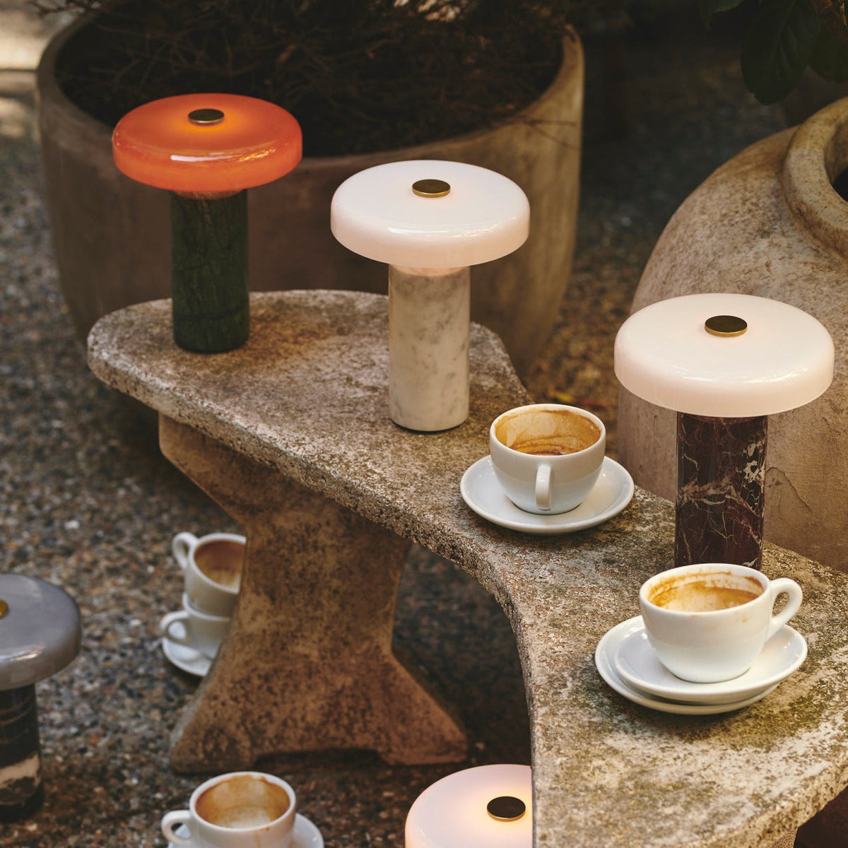 Trip Table Lamp in Moss / Amber, Carrara / Opal and Burgundy / Opal on a stone bench