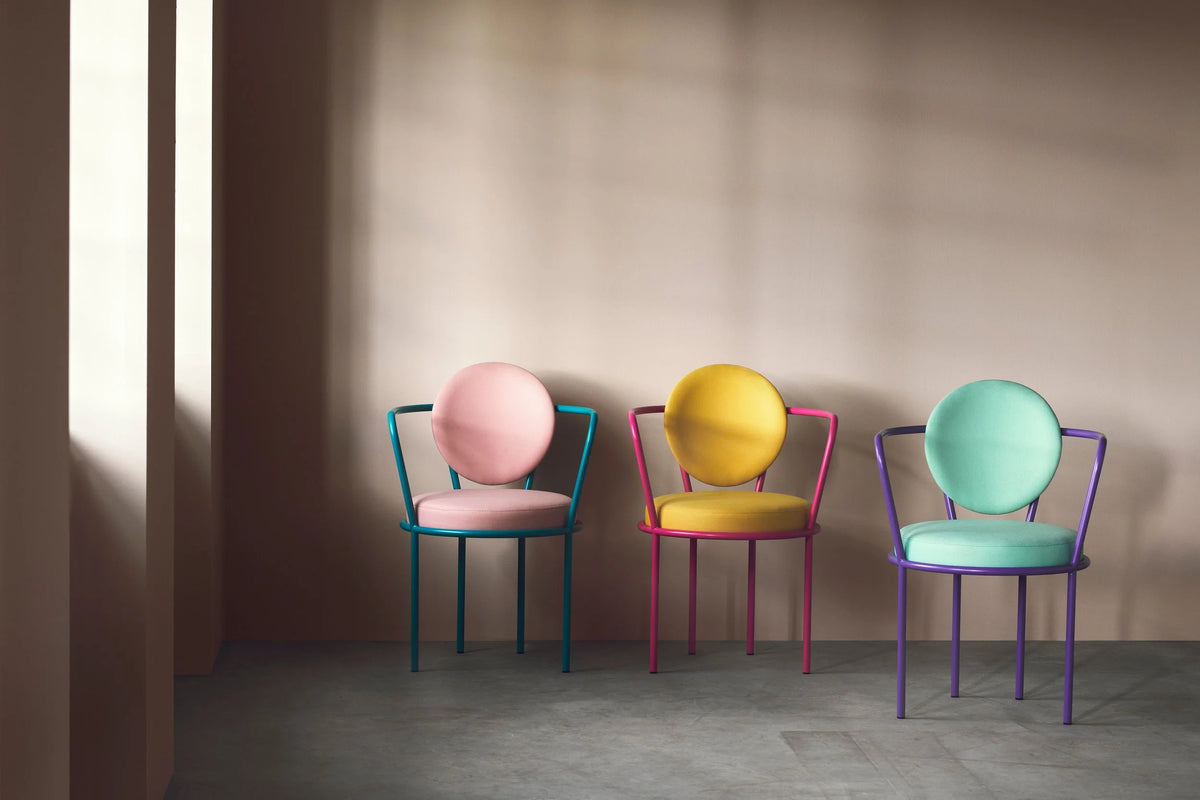 Three dining chairs in pink, yellow and mint against a blush wall