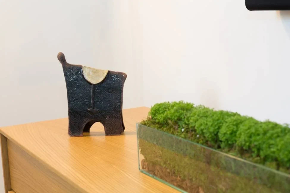 Ceramic sculpture and a glass planter of moss on a wooden sideboard